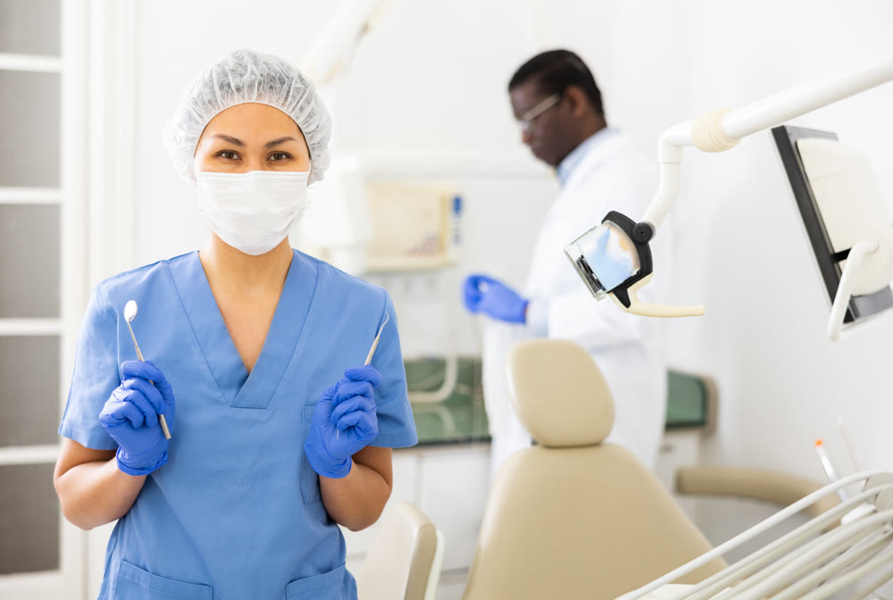Female dentist standing in dental office with tools in hands