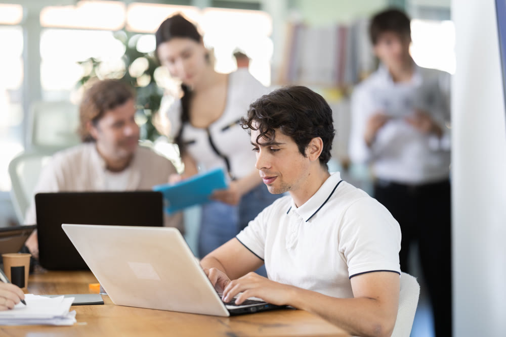 Young office worker works on laptop in modern open-plan office