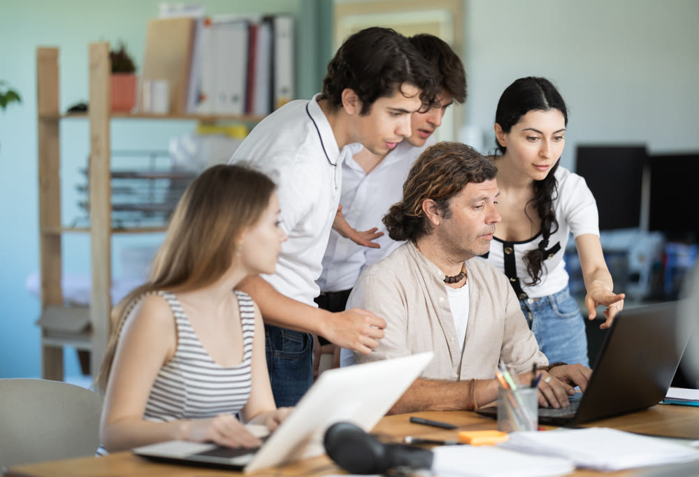 Team businessmen discusses business project while gathered around laptop in company office