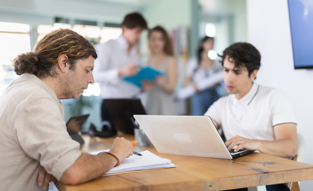 Employees working with laptops and paper documents in office