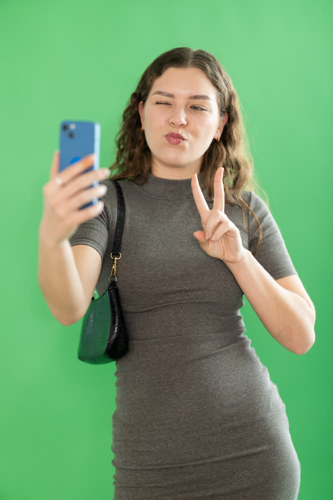 Csmiling pretty girl takes selfie on green background. Chroma key compositing.