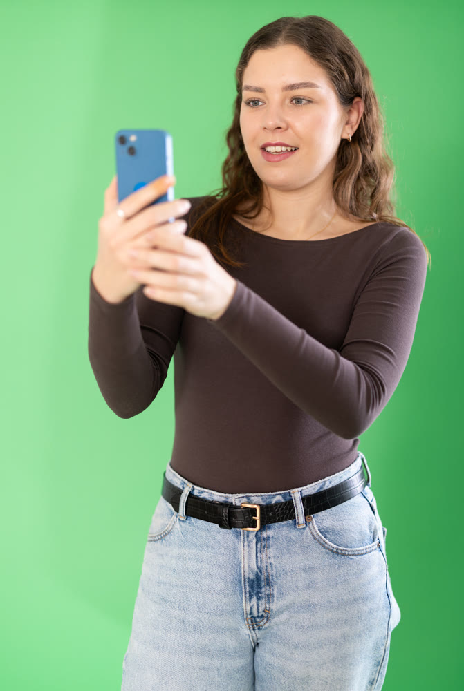 Young woman taking photo or scanning QR code in front of green screen
