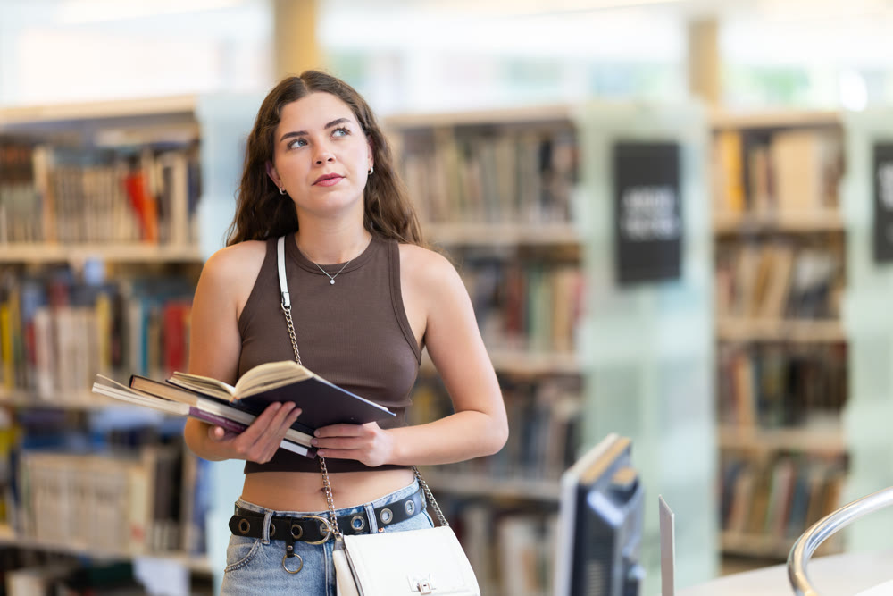 Young female student reading book in library