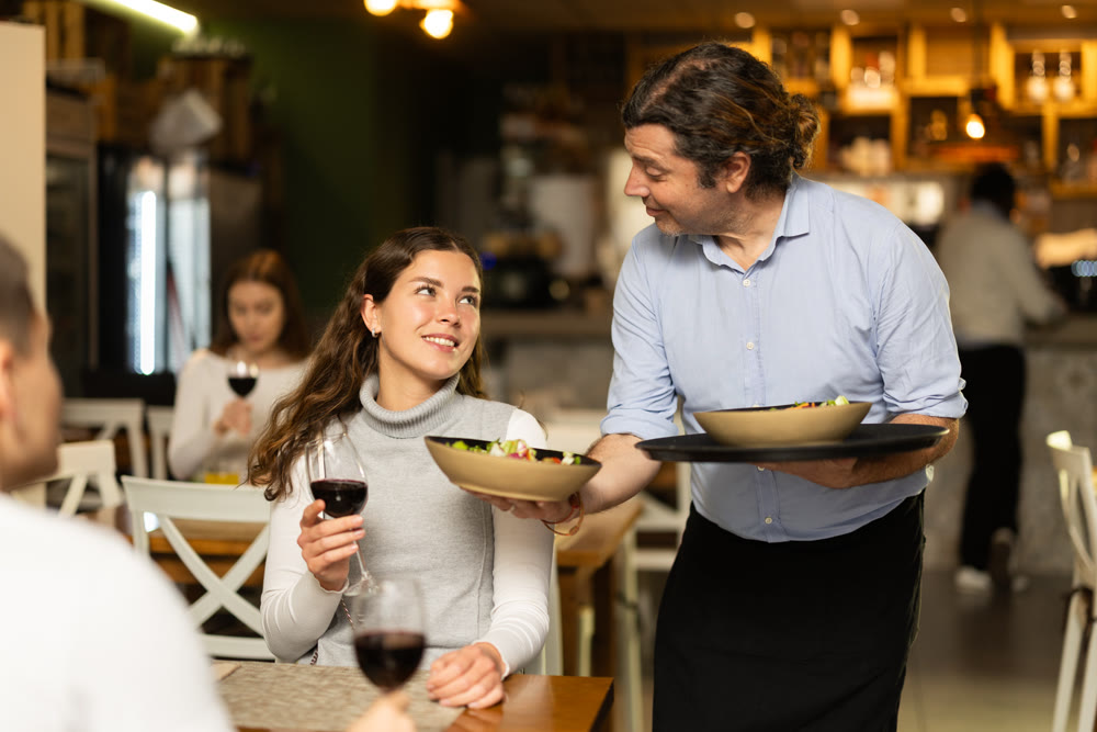 Man waiter serves cafe establishments girl visitor, puts food on table.