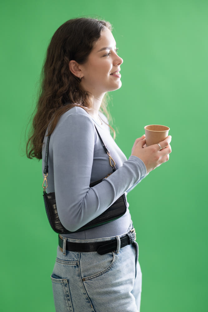 Young woman drinking coffee in front of green screen