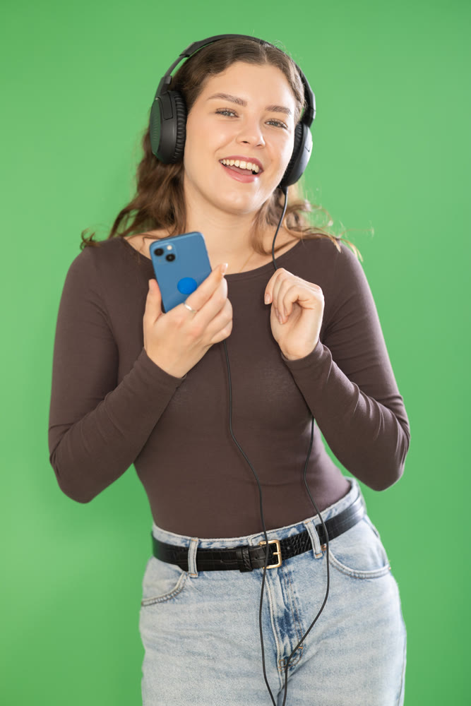 Young woman listening to music with headphones in front of green screen