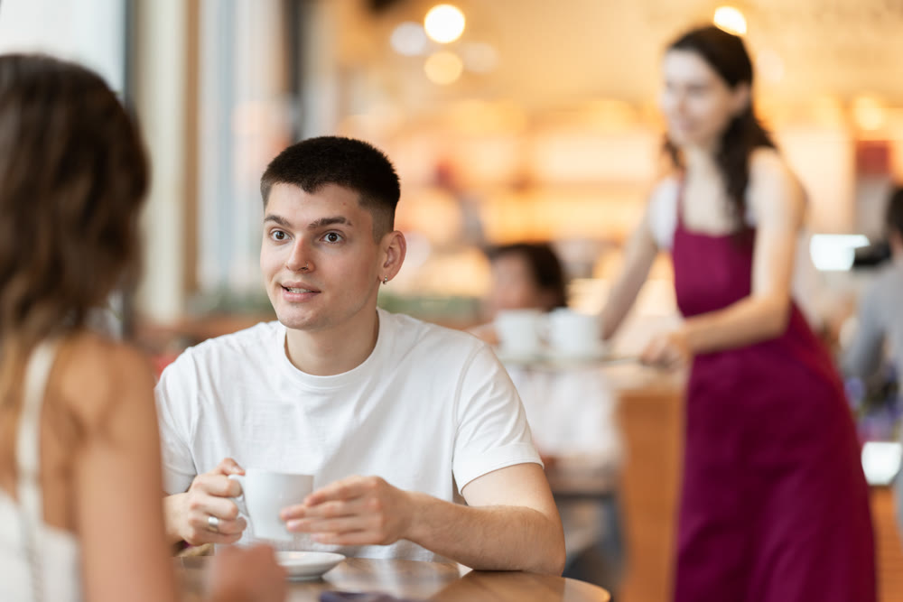 Guy in cafe sits opposite female companion, has nice conversation