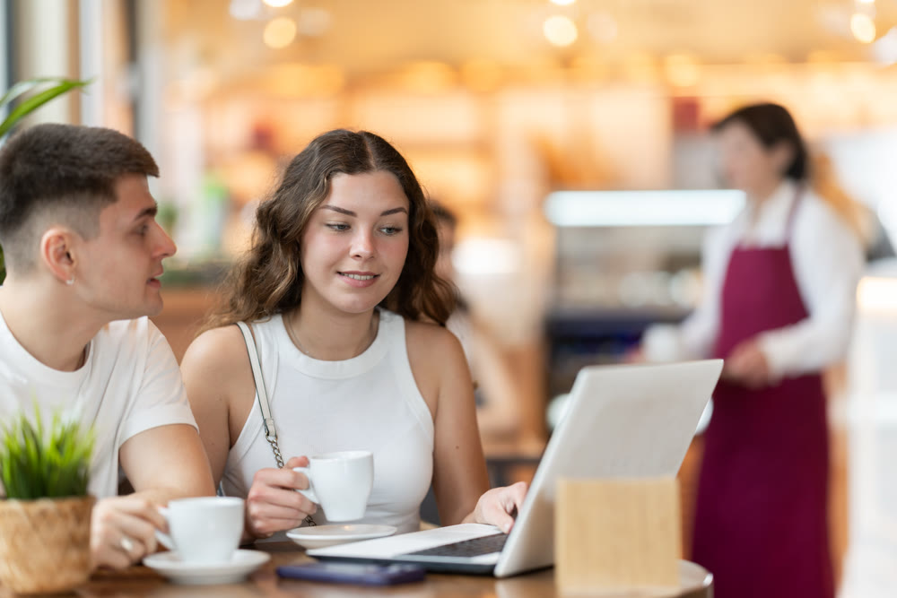 Girl and guy freelancers in cafe with laptop drinking coffee