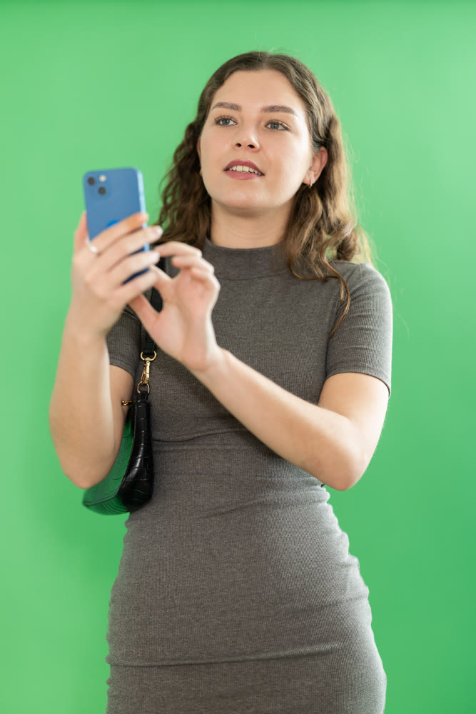 Happy girl scans QR code or takes photo with a smartphone. Green background. Chroma key compositing