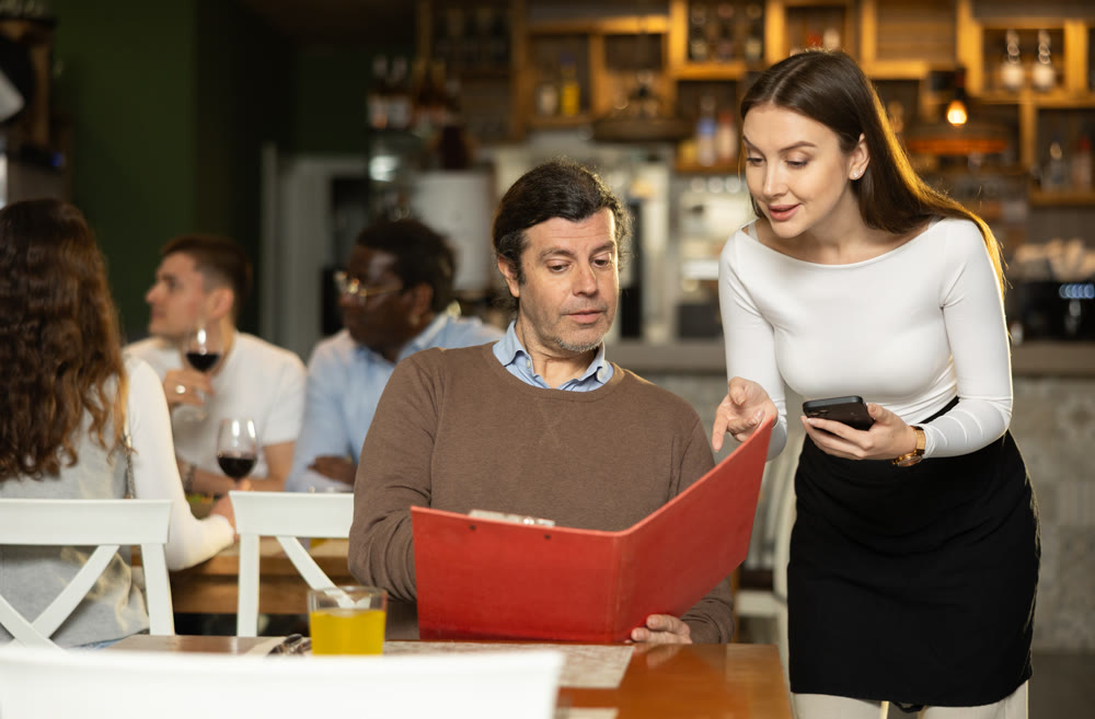 Girl waiter communicates with male customer, answers questions about composition of dish of day