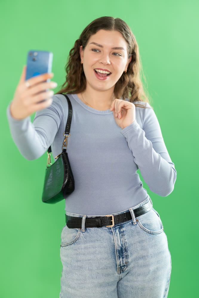 Young woman taking selfie in front of green screen