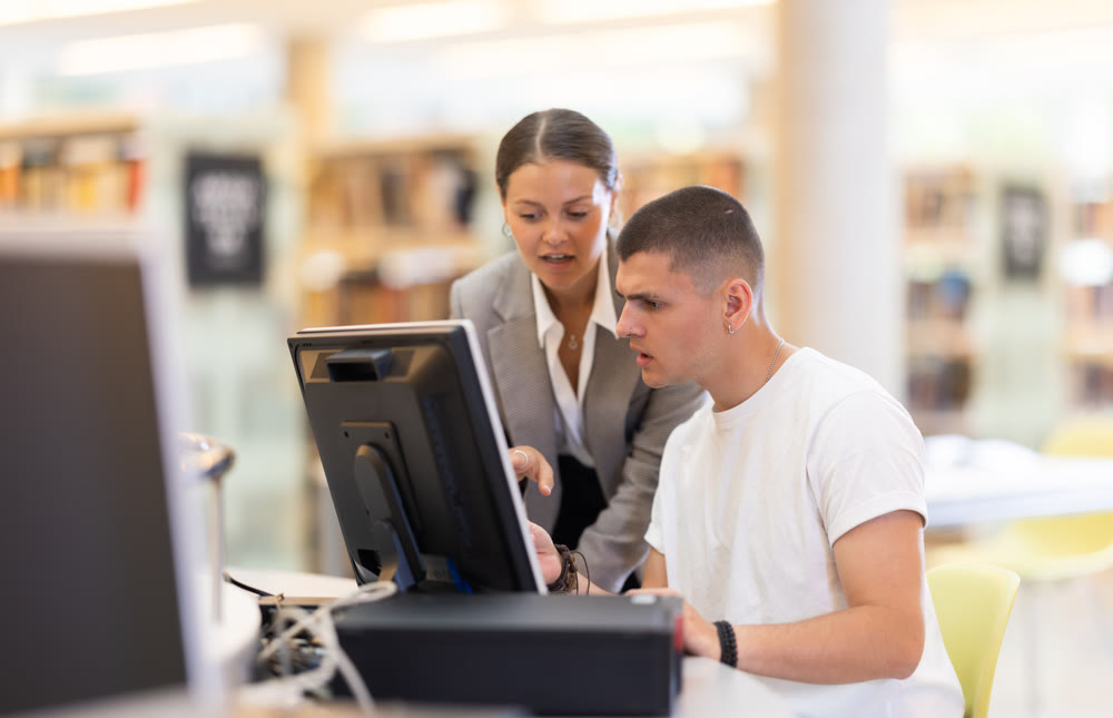 Female student helping guy student work on computer