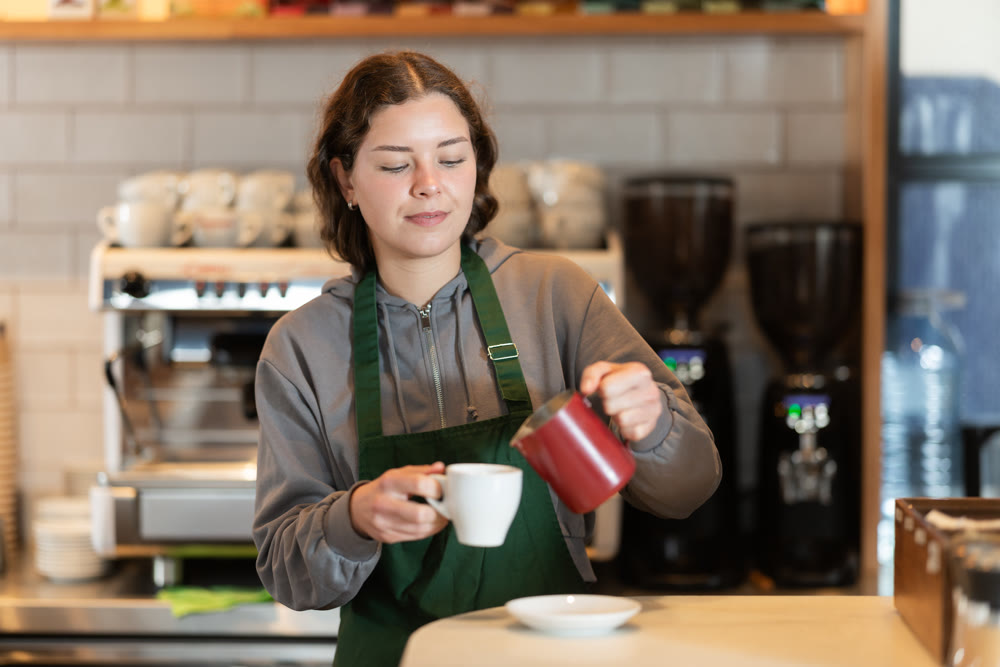 Young female barista pouring coffee in cafe