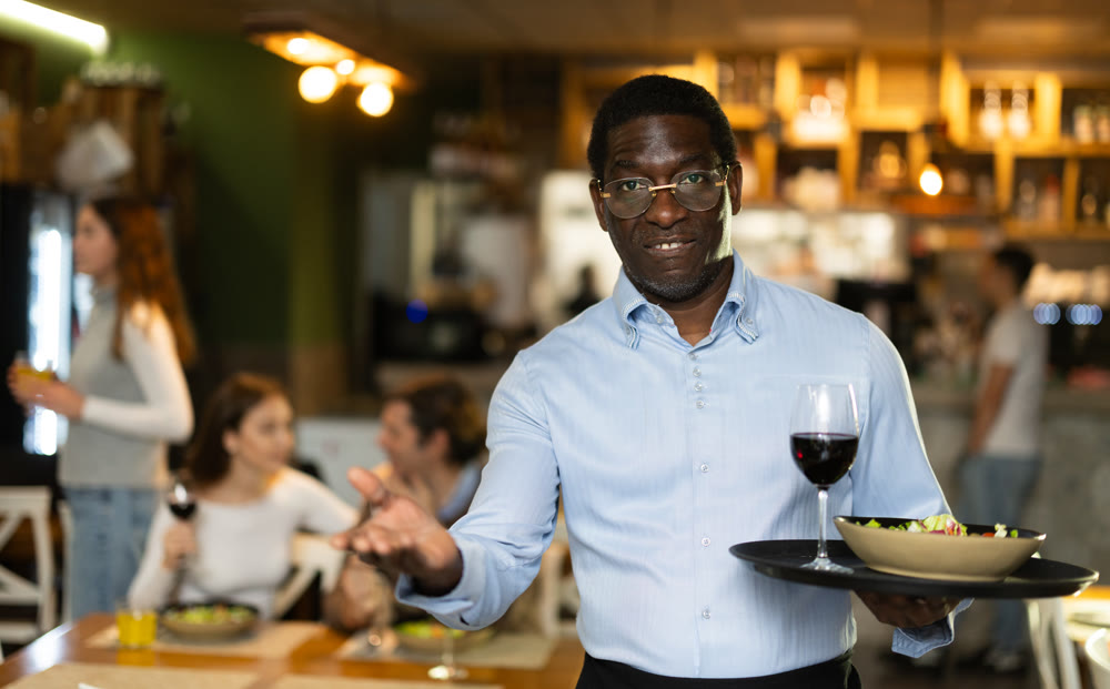 African waiter with a tray in his hands offers dinner in a restaurant
