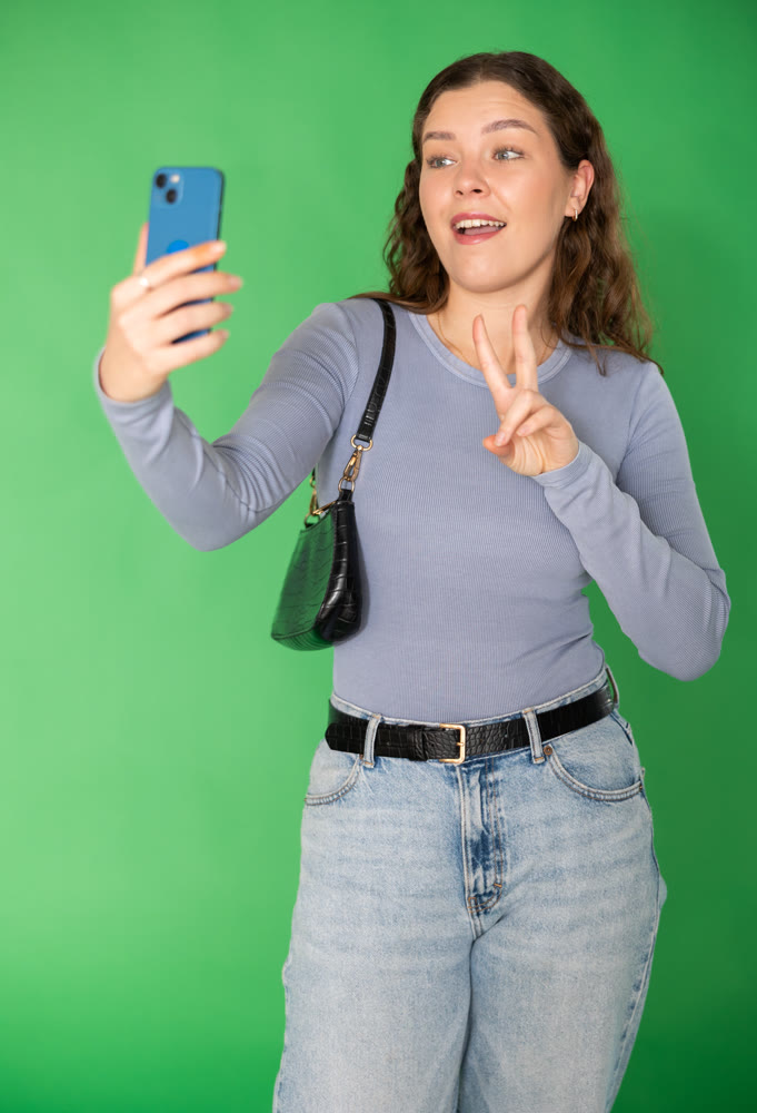 Young woman taking selfie in front of green screen