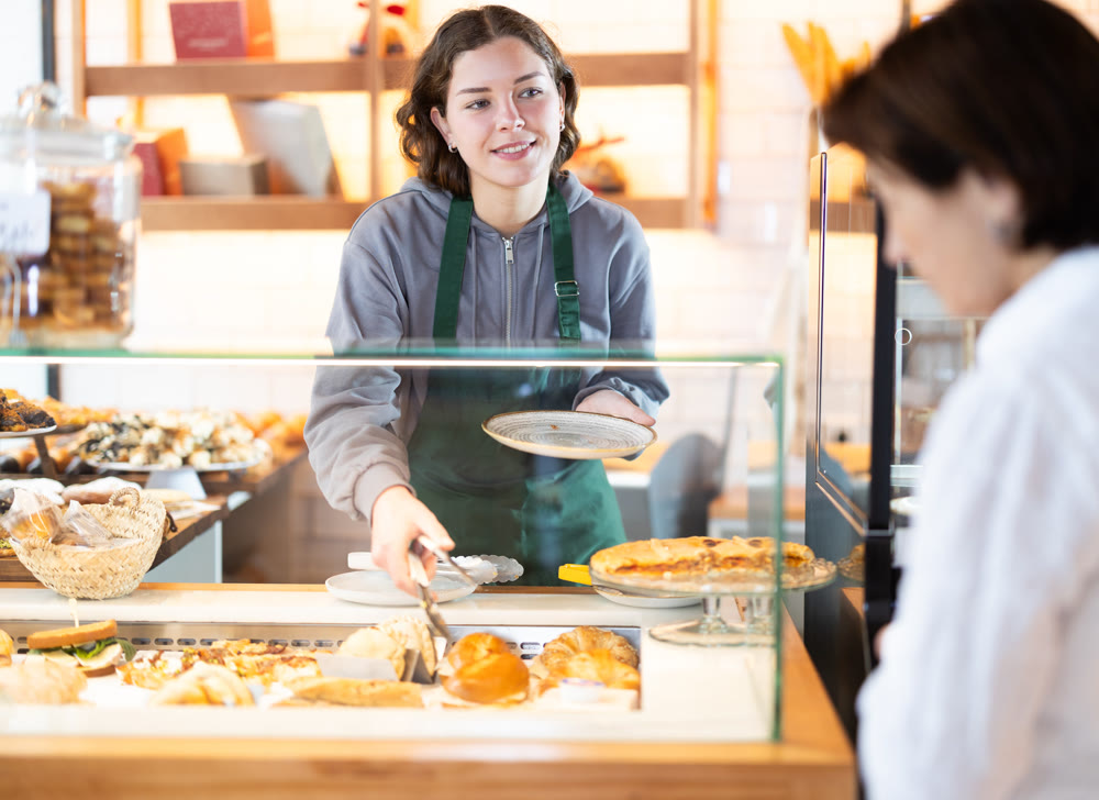 Young woman giving pastry to client in cafe