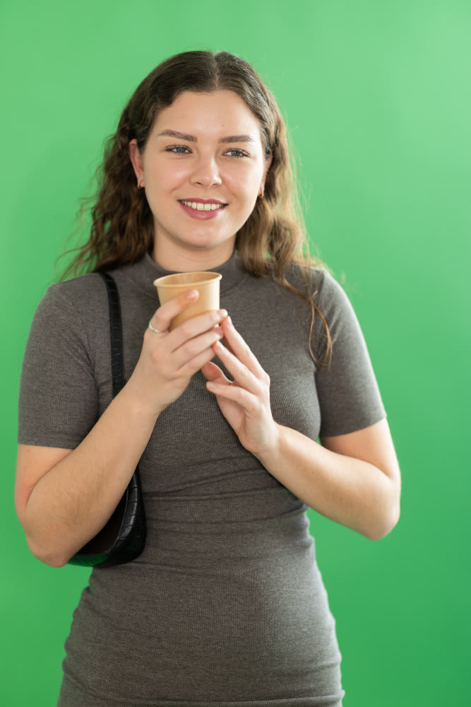 Young woman drinking coffee in front of green screen