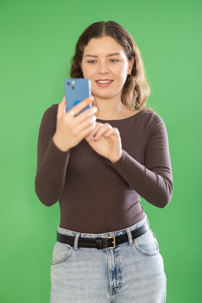Young woman taking photo or scanning QR code in front of green screen