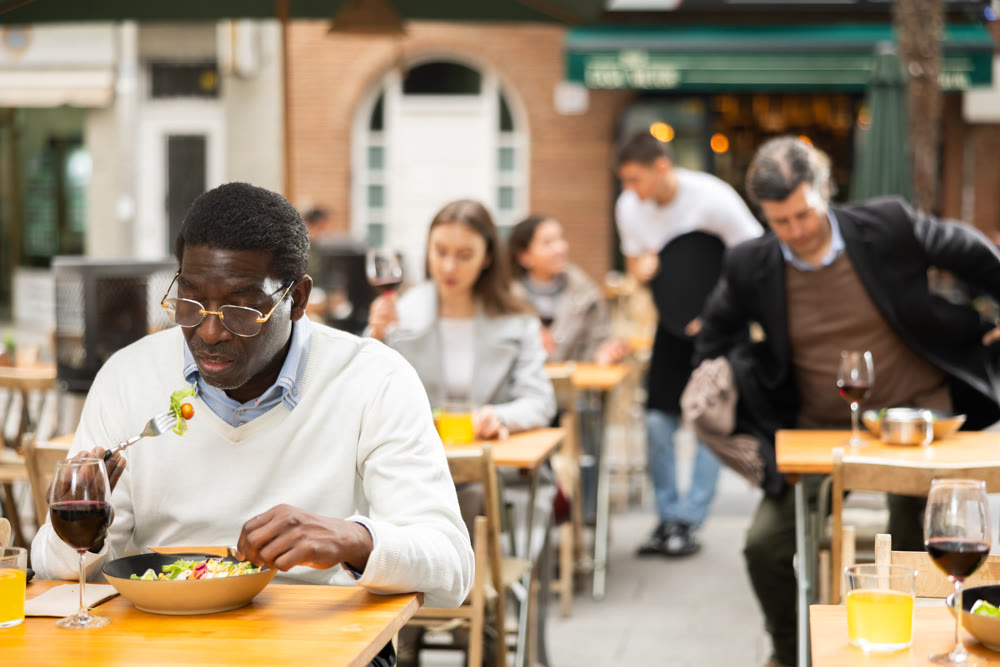 On open area of cafe, African man in restaurant eating salad