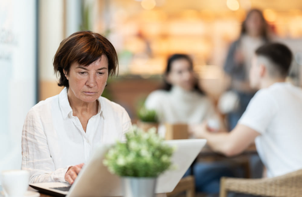 In cozy cafe hall, freelance mature woman using laptop and drinks coffee.