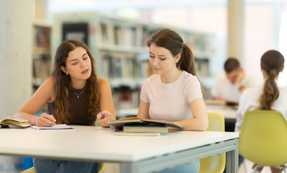 Two female student friends studying for exams together in university library