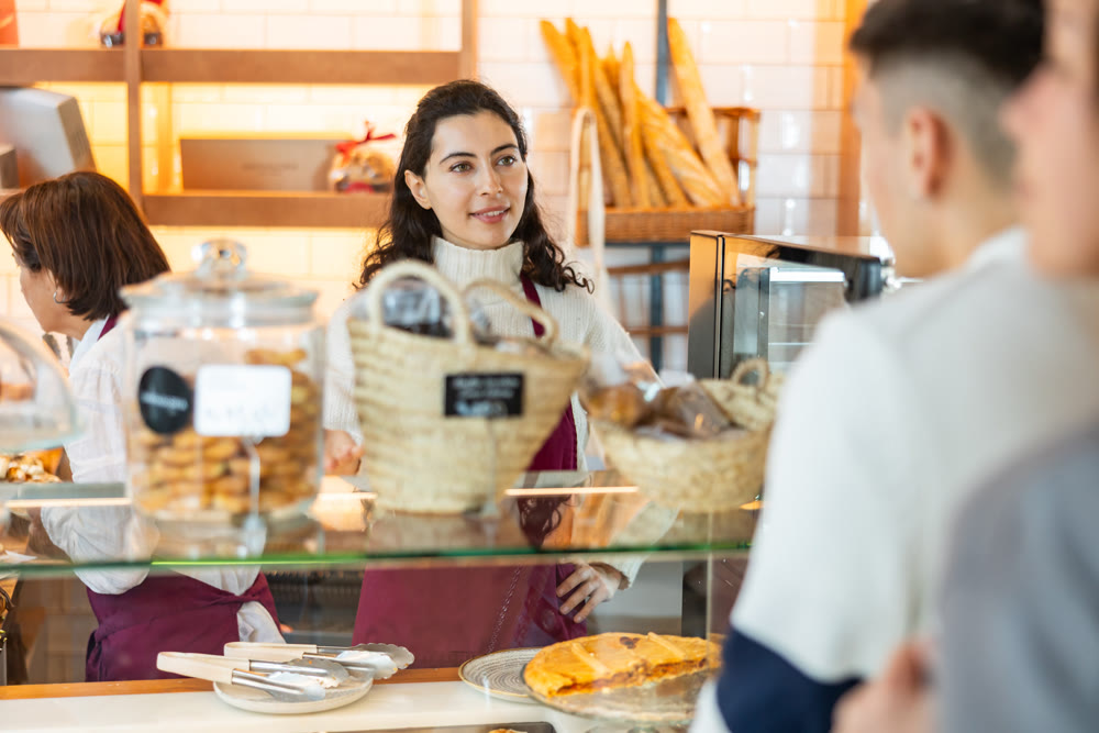 Seller in an apron is standing in a coffee shop and talking to a client
