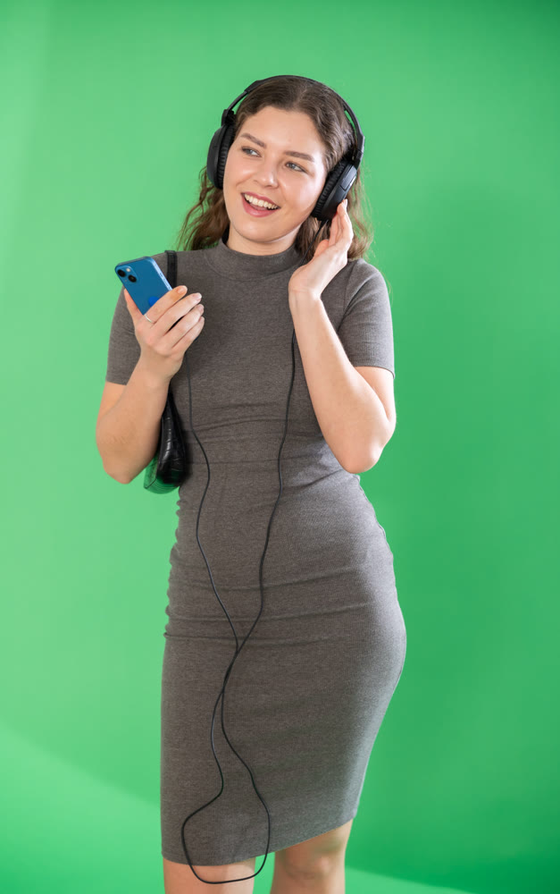 Young woman listening to music with headphones in front of green screen