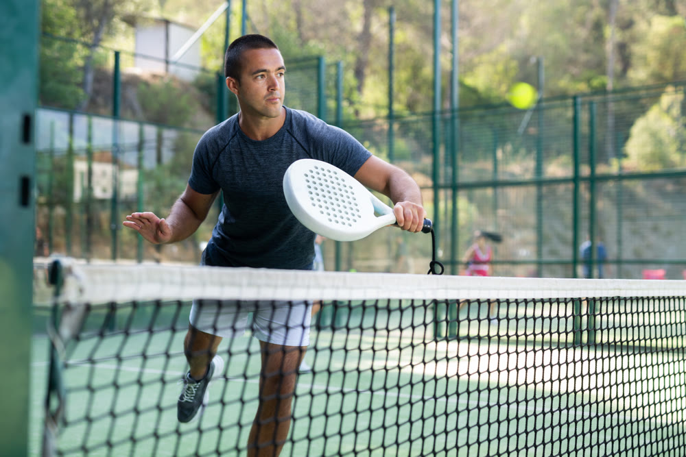 Athletic man plays padel. View through tennis net outdoor