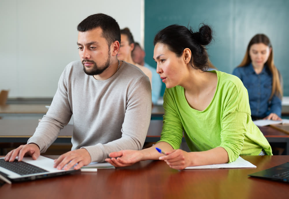 Man and woman helping each other to solve problem on laptop while studying in university class