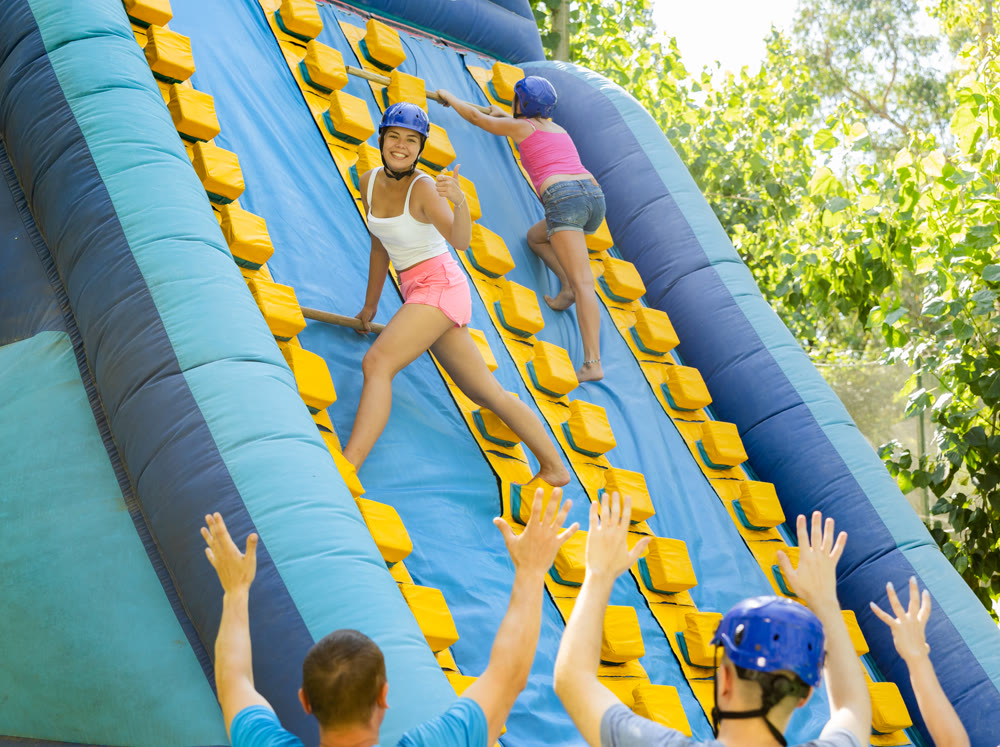 Cheerful girl climbing on inflatable slide with wooden poles