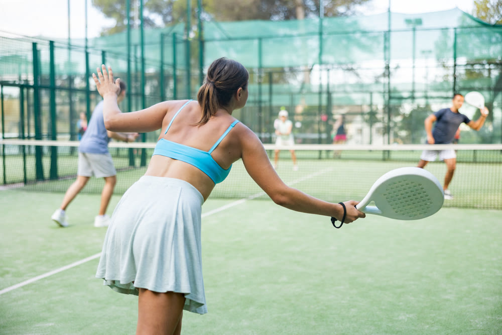 Sportive slim woman with racquet playing padel in court. View from back