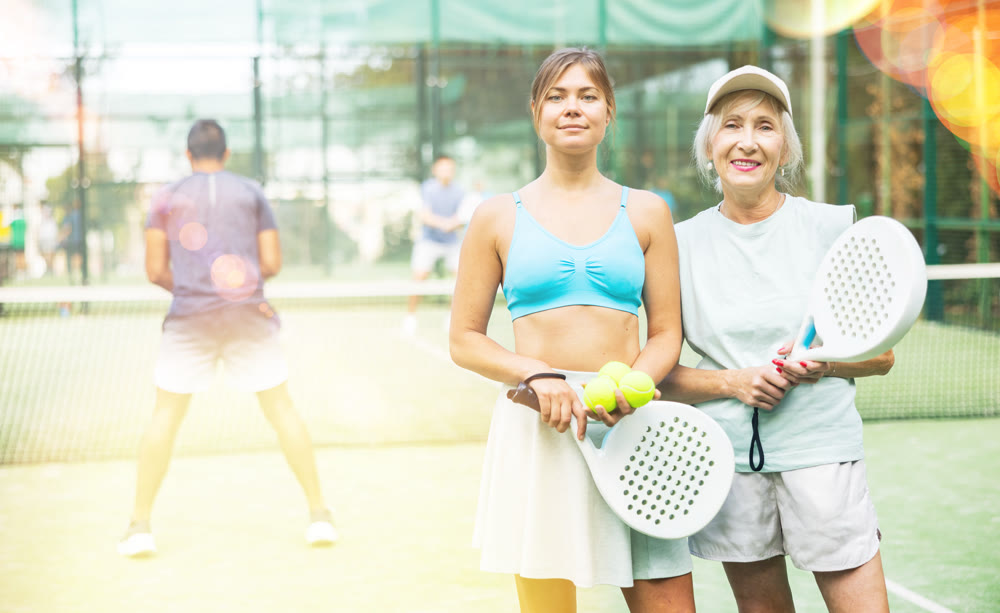Sports two women with padel rackets posing on tennis court outdoor