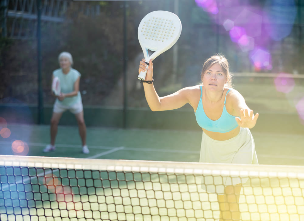 Sporty young woman playing padel on open court on summer