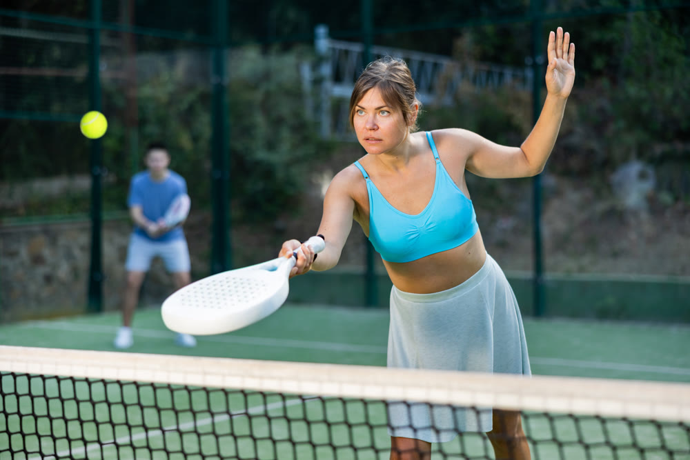 Sporty young woman playing padel on open court on summer