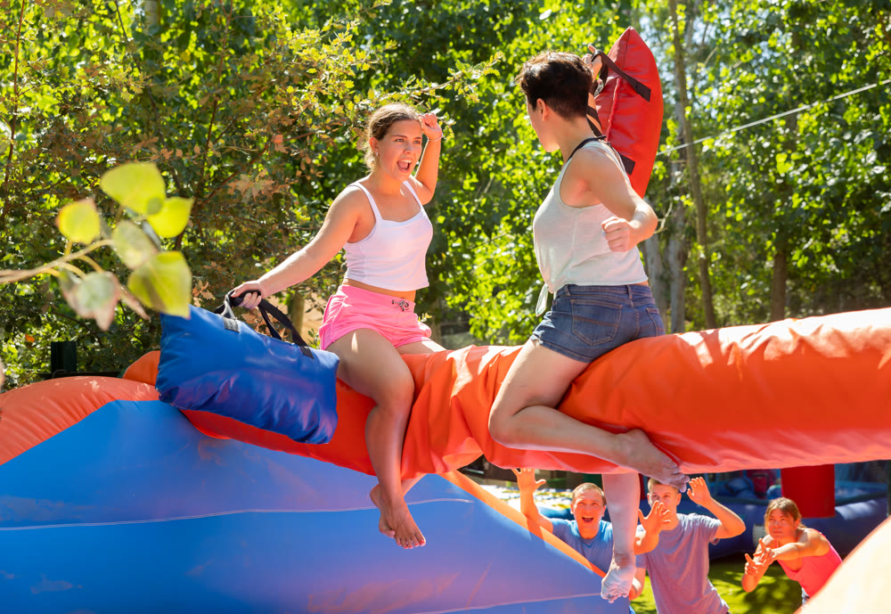 Happy girl funny pillow fighting on inflatable log with female friend