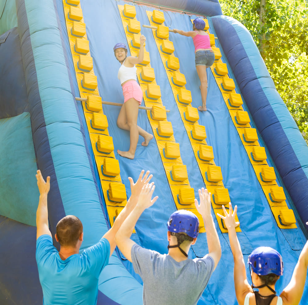 Women using sticks to reach top of slide in adventure park