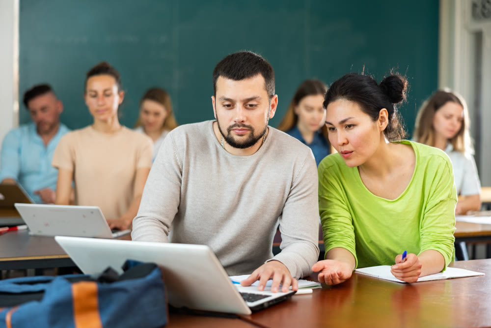 Woman and man university students using laptop and exercising together