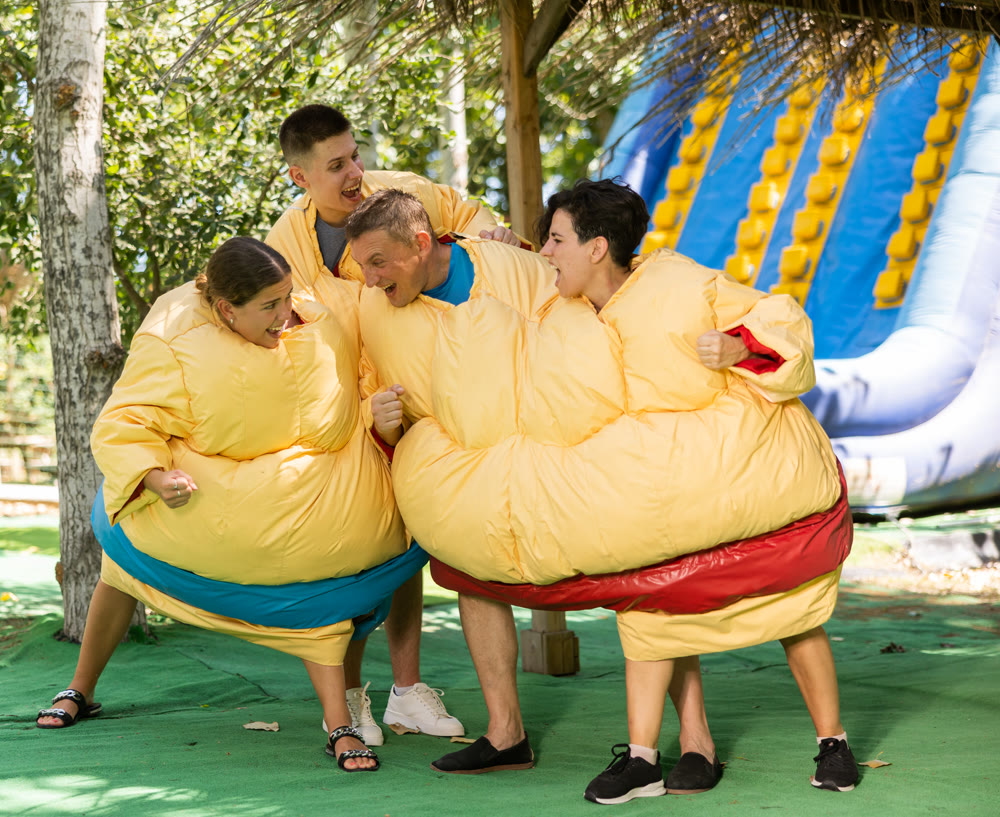 Playful adults having fun wrestling by pairs in inflatable sumo suits