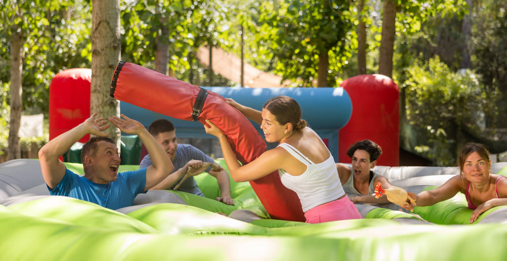 Cheerful girl fighting off friends with inflatable log while guarding toy chickens