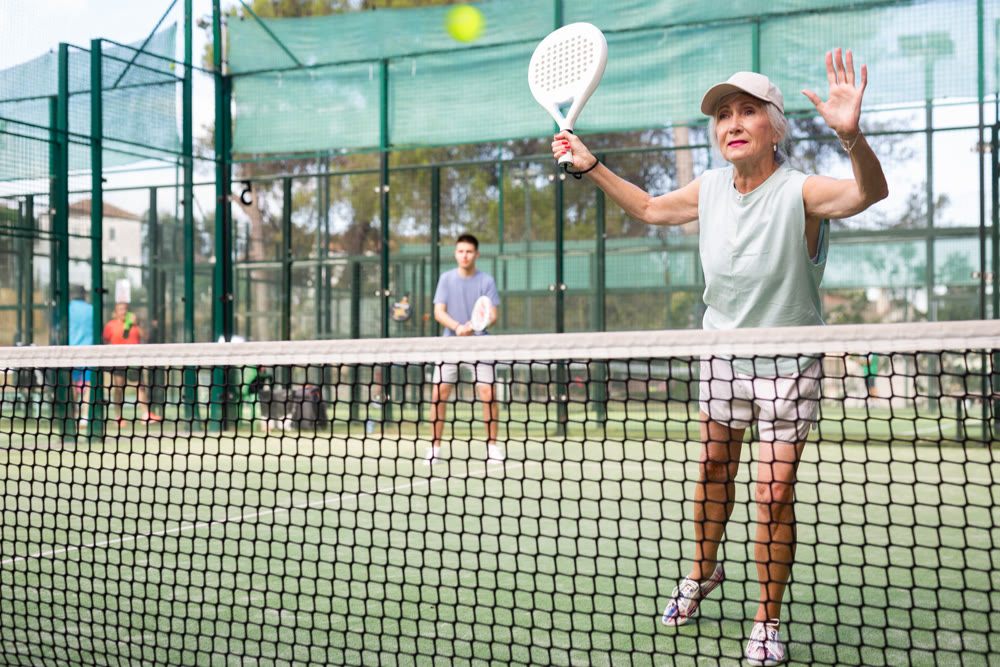 Aged woman playing friendly paddleball match on outdoor court