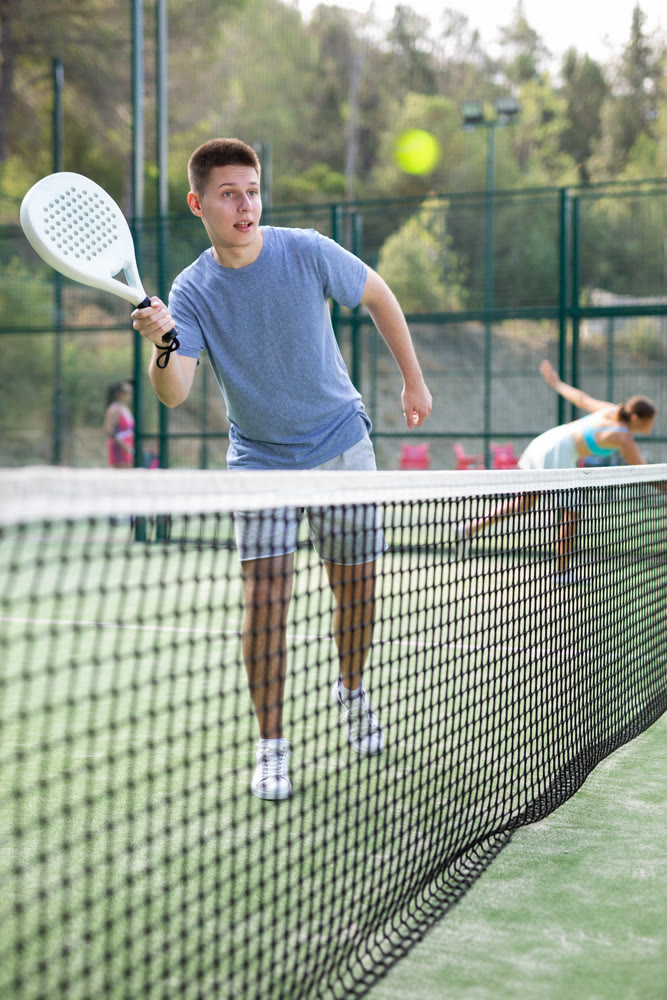 Sporty young guy playing padel on open court in summer