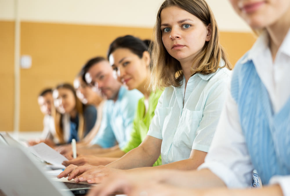 Portrait of womens and mens studying in classroom, listening to teacher and writing in notebook
