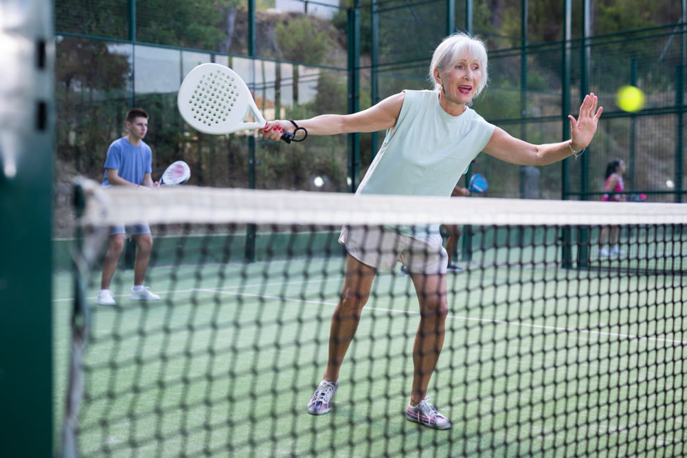 Active elderly woman playing padel tennis on open court