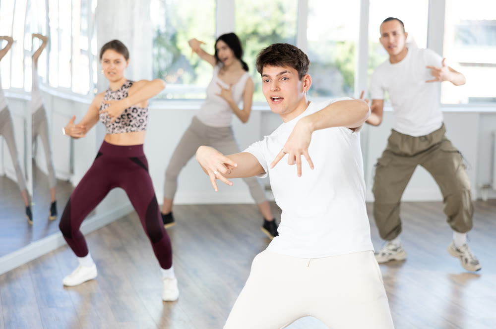 Guy enjoys active dancing, learns new movements, moves synchronously with participants of lesson