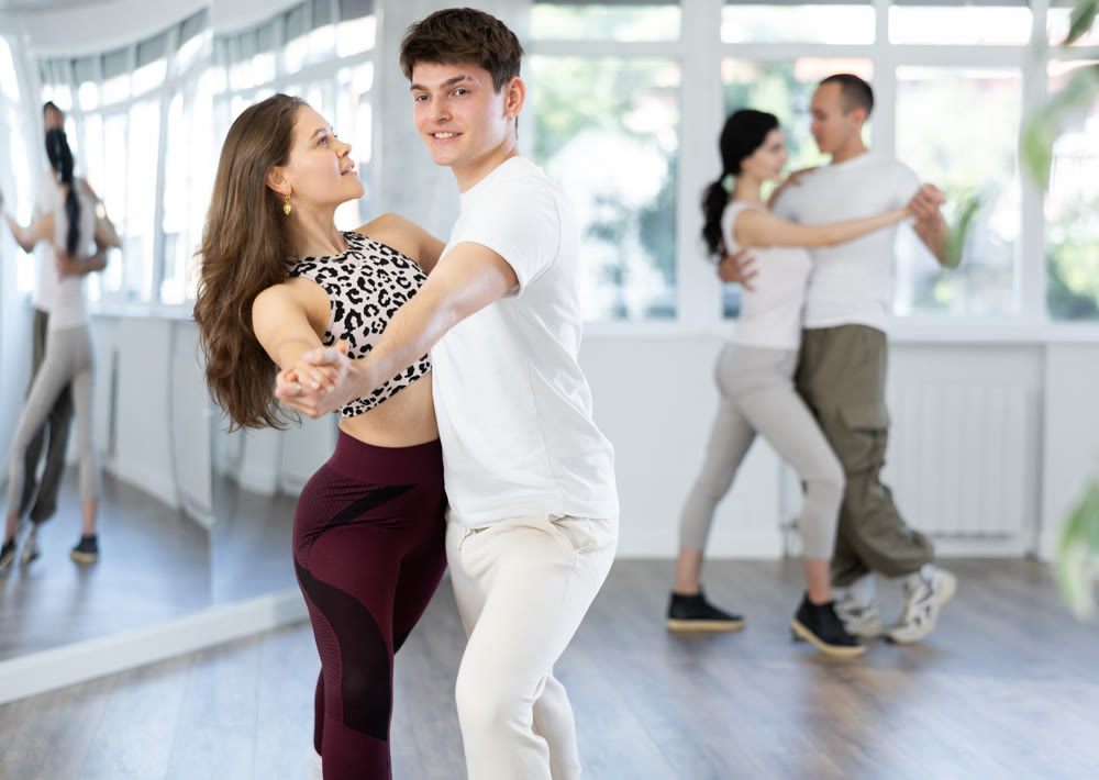 Young girls dancing together with guy slow ballroom dances in pairs in ball room at dance salon