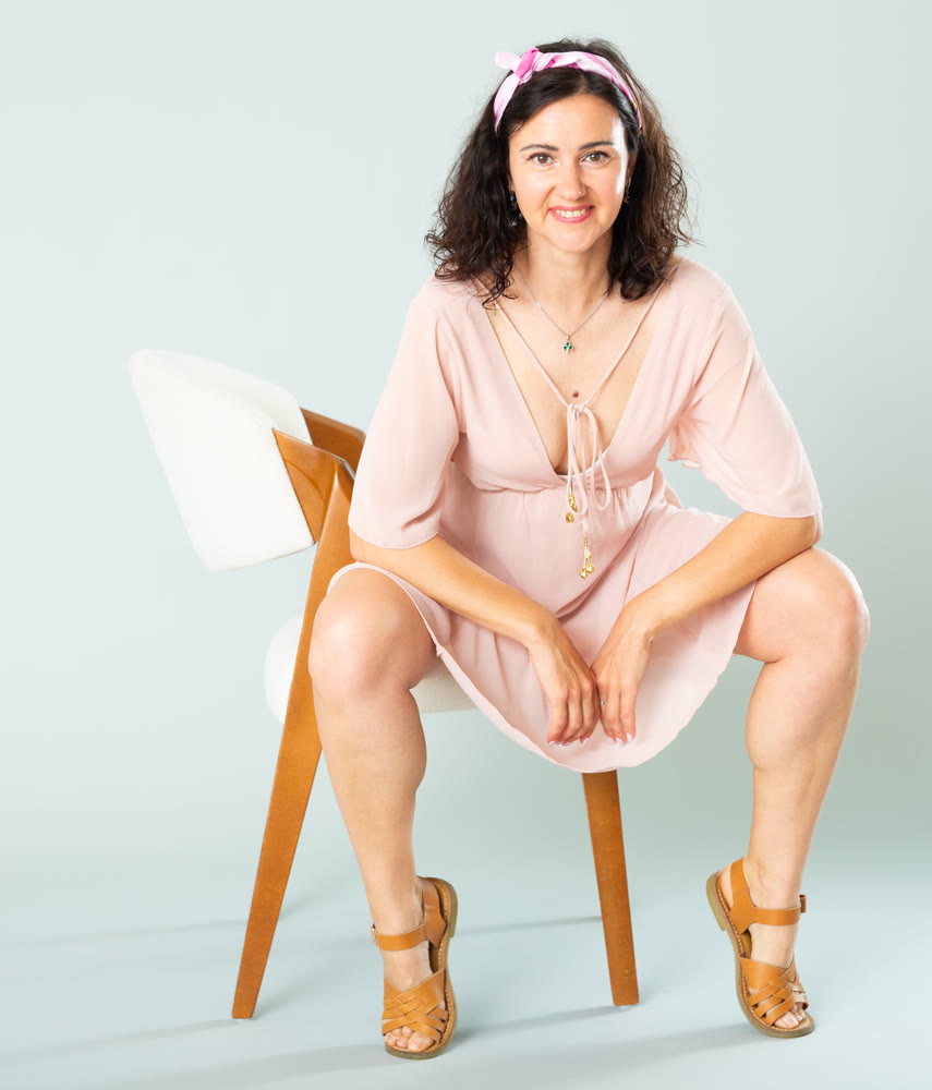 Woman in pink dress posing on chair against background of wall