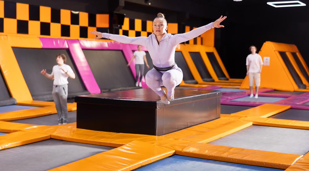 Middle-aged woman in sport clothes high jumping in trampoline arena