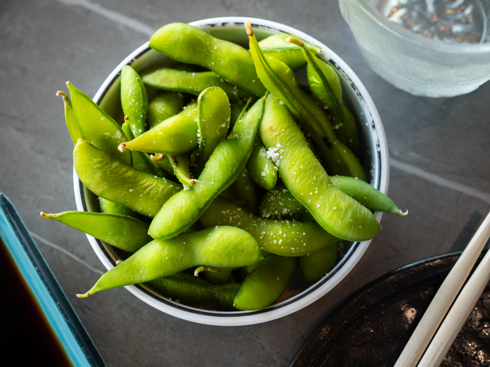 Steamed edamame sprinkled with sea salt on dark stone board, top view