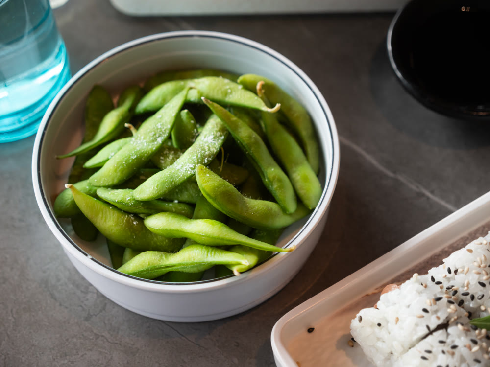 Steamed edamame sprinkled with sea salt on dark stone board, top view