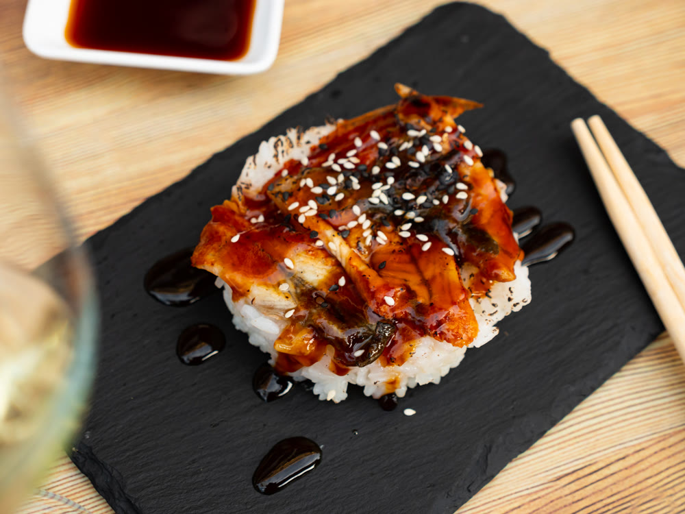 Japanese appetizer with fried eel, saucer and rice on a stone stand with chopsticks